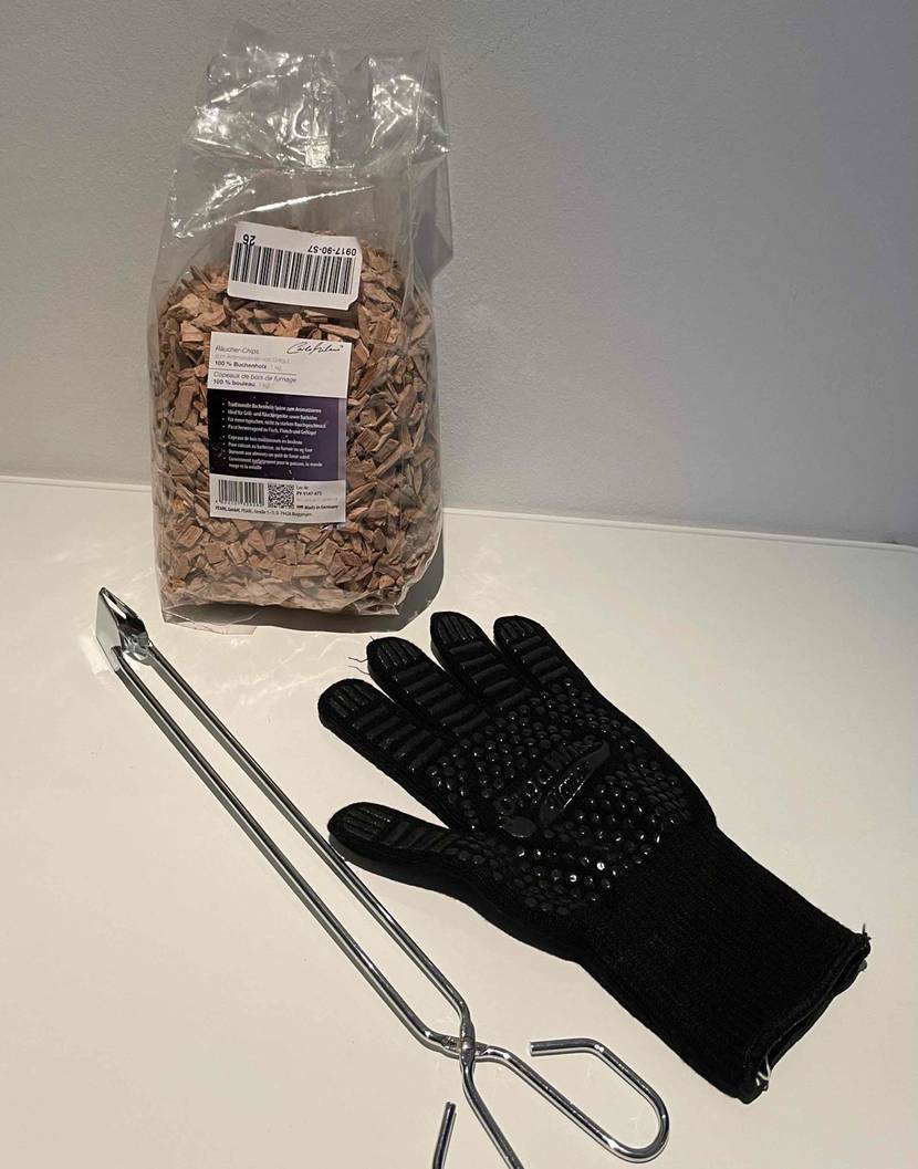 Eine Grillzange im Test liegt neben Grillhandschuh und Räucherchips.