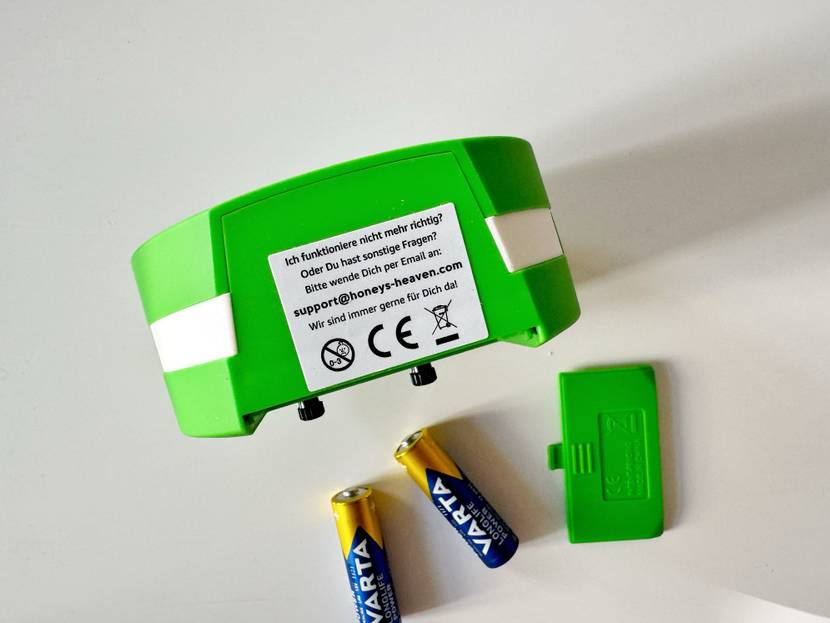 Unterseite eines getesteten Kinderweckers mit Aufkleber mit Supporthinweis und nebenliegendem Batteriefachdeckel und Batterien.