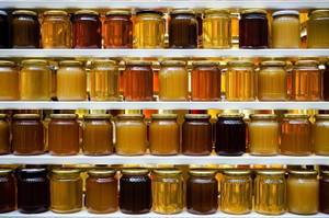 verschiedene honigsorten in gläsern auf mehreren regalbrettern