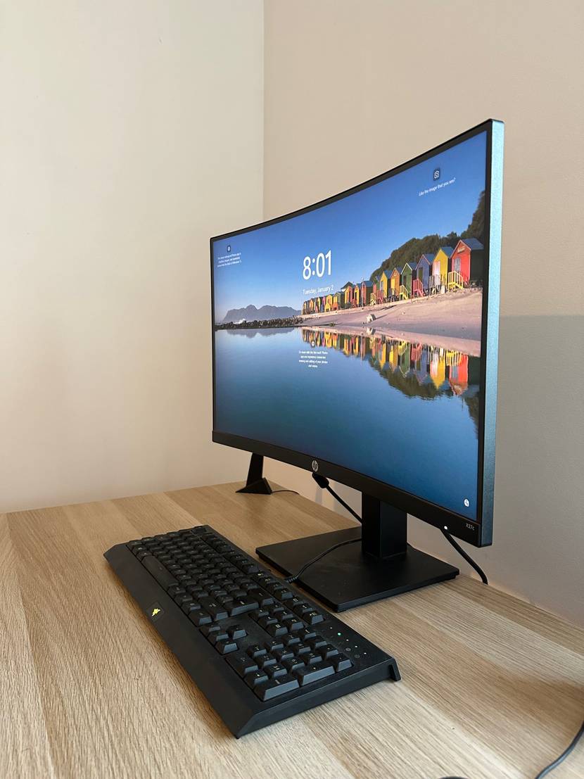 Seitenansicht eines eingeschalteten, getesteten Curved Monitors, der auf einem hellen Schreibtisch steht.