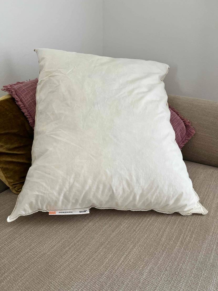 Ikea Kopfkissen getestet: weißes Kissen liegt auf zwei anderen farbigen Kissen in einem Sofaeck.