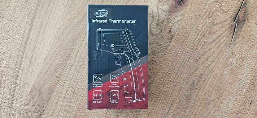 Die Originalverpackung eines getesteten Infrarot-Thermometers liegt auf einem Holzboden.