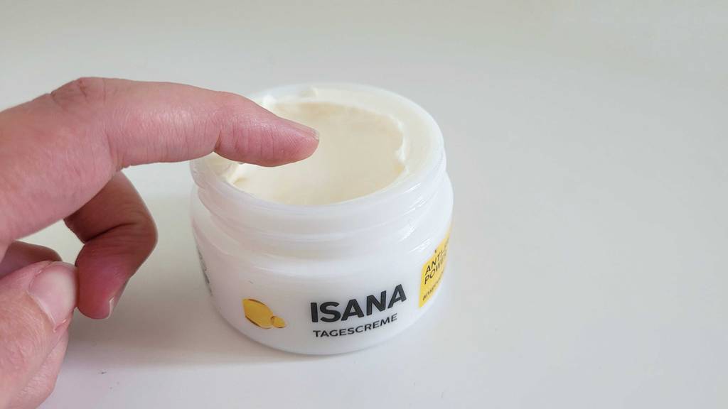 Finger in einer geöffneten Tagescreme-Dose, die auf dem Tisch steht