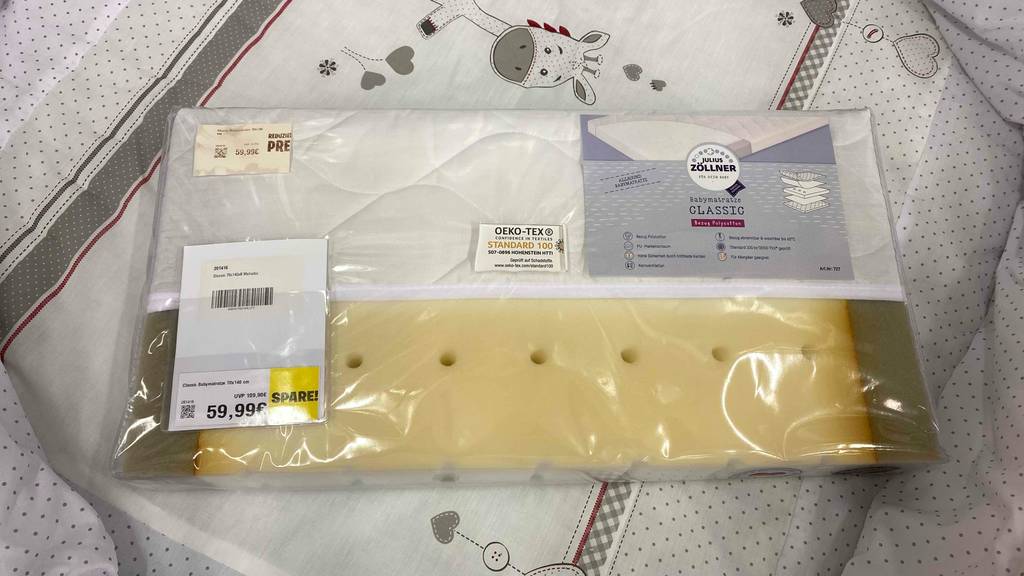 Babymatratzen-Test: ein Schaumstoff-Modell der Marke Julius Zöllner liegt in seiner durchsichtigen Originalverpackung inklusive Preisschild auf einem Bettenbezug.