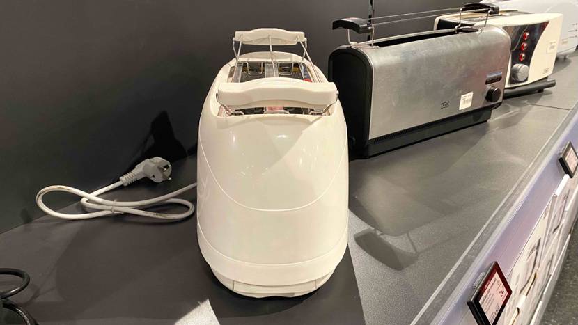 Ein getesteter Langschlitztoaster mit der schmalen Seite nach vorne auf einem dunklen Regal neben anderen Produkten stehend.
