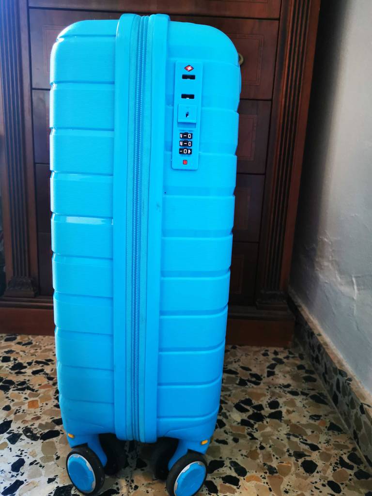 Ein türkisfarbener, getesteter Koffer, inklusive TSA-Schloss, steht auf seinen Rollen vor einem braunen Holzschrank.