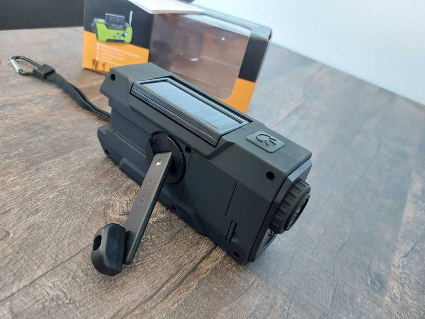 Getesteter Kurbelradio mit manuellem Sendersucher liegt auf einem Holztisch neben der Verpackung. 