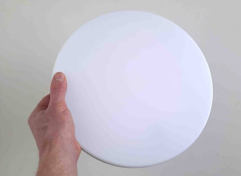 Im Test: Eine Hand hält eine LED-Deckenleuchte vor eine helle Wand.