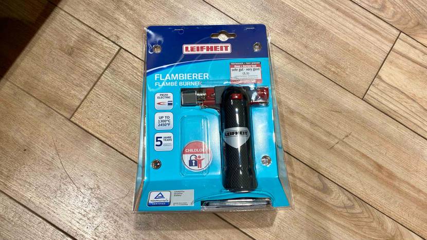 Flambierbrenner getestet: Ein originalverpacktes Gerät liegt auf einem Holzboden.