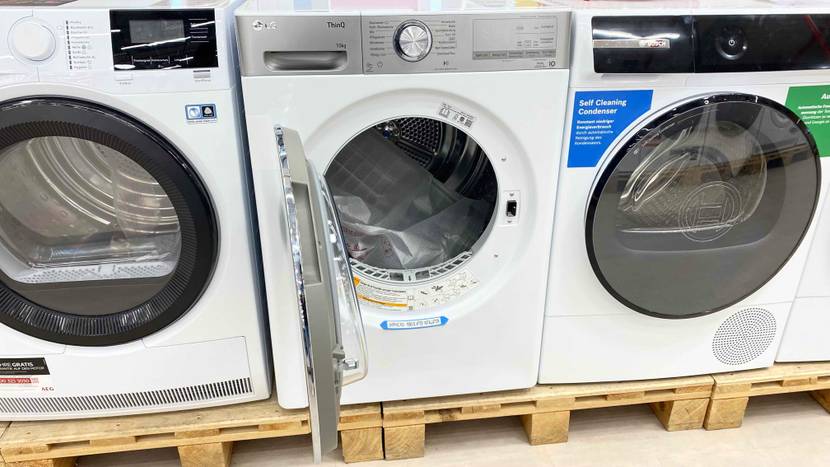 Wärmepumpentrockner im Test: Ein weißes Modell von LG steht mit geöffneter Tür zwischen zwei anderen Wärmepumpentrocknern auf Holzpaletten.
