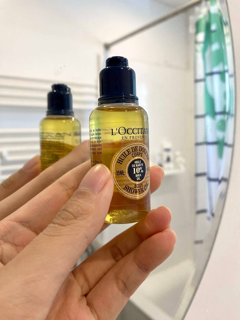 Kleine Duschölflasche in der Hand, Dusche im Hintergrund.