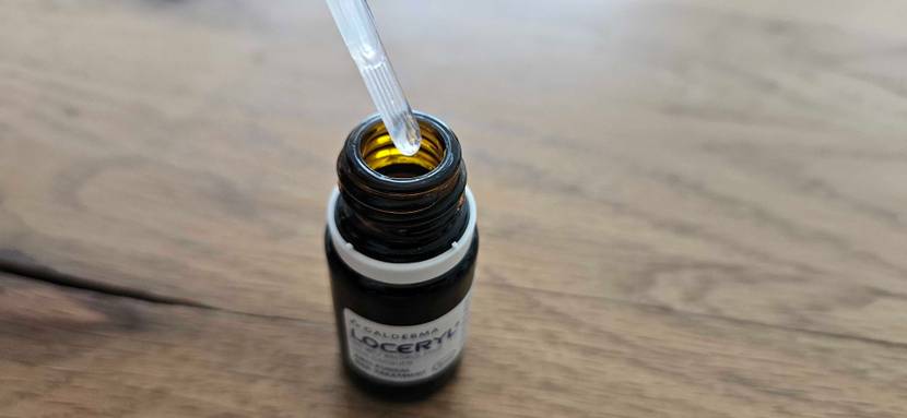 Loceryl-Mittel gegen Nagelpilz im Test: Ansicht von schräg oben auf eine Pipette über einer kleinen, lichtdichten Braunglas-Flasche auf Holz.
