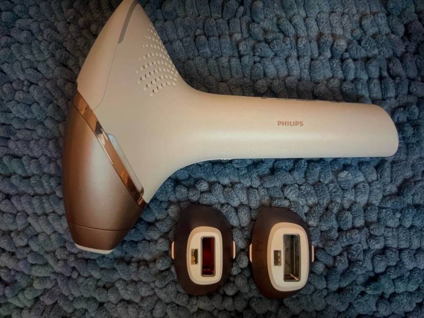 Weißes IPL-Gerät im Test: Philips Licht-Haarentfernungsgerät Lumea Prestige liegt neben zwei unterschiedlichen Aufsätzen auf einem blauen Flauschteppich.