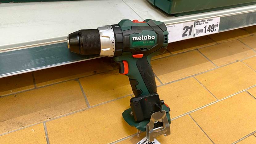 Ein grün-schwarzer Metabo Akku-Bohrschrauber im Test steht ohne Akku auf gelben Fliesen in einem Verkaufsbereich.