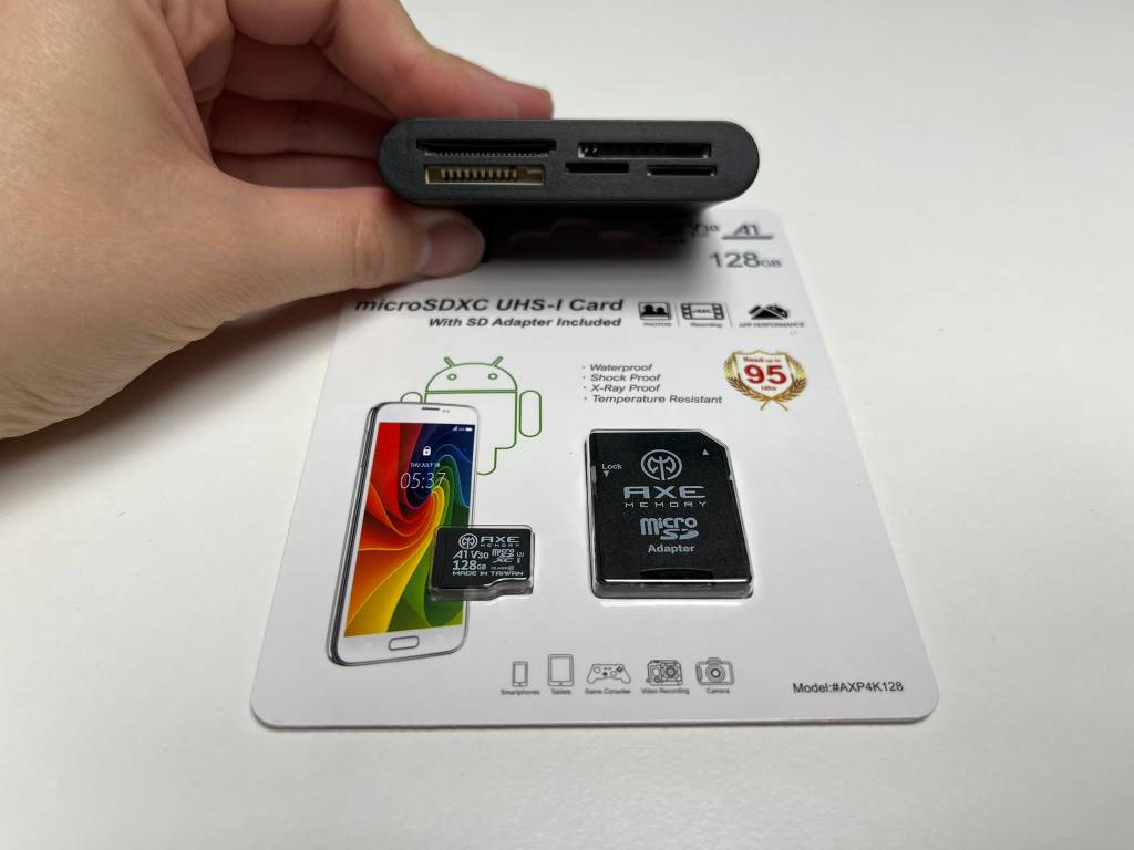 Hand hält Lesegerät während eine Micro-SD-Karte in Verpackung auf dem Tisch darunter liegt.