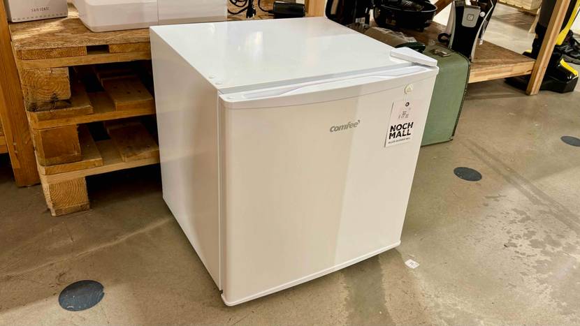 Ein getesteter Mini-Kühlschrank von schräg vorne auf einem Betonboden vor Holzpaletten stehend.
