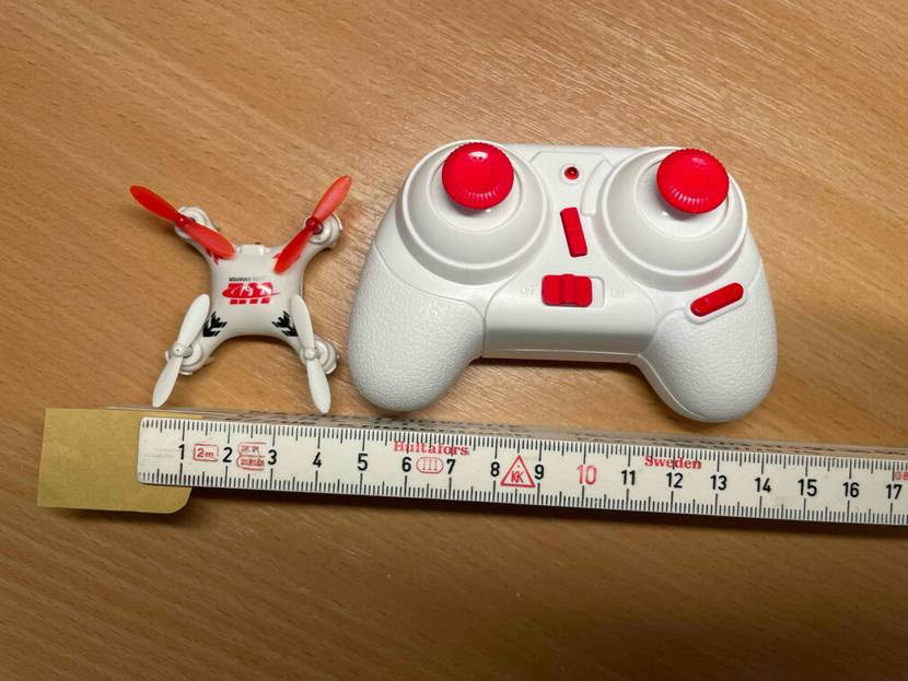 Auf einer Holzfläche liegen der Mini-Quadrocopter im Test neben seinem Controller und einem Lineal.