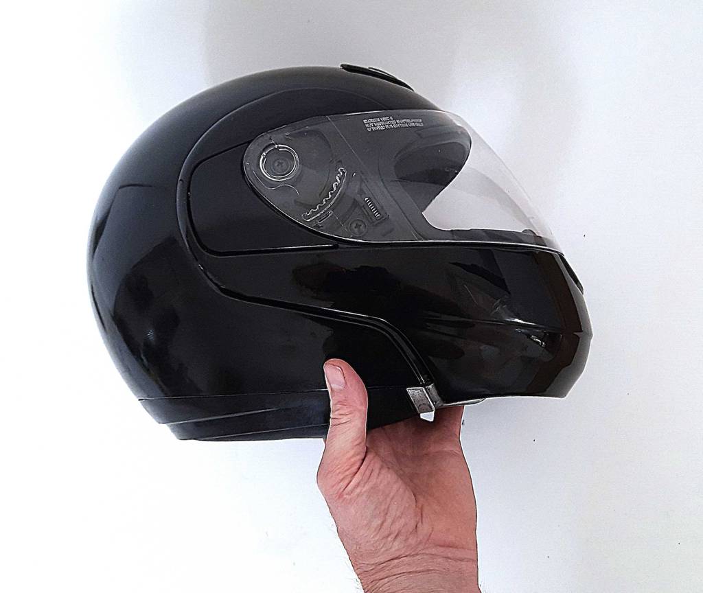 Eine Hand hält einen getesteten Motorradhelm in Seitenansicht.