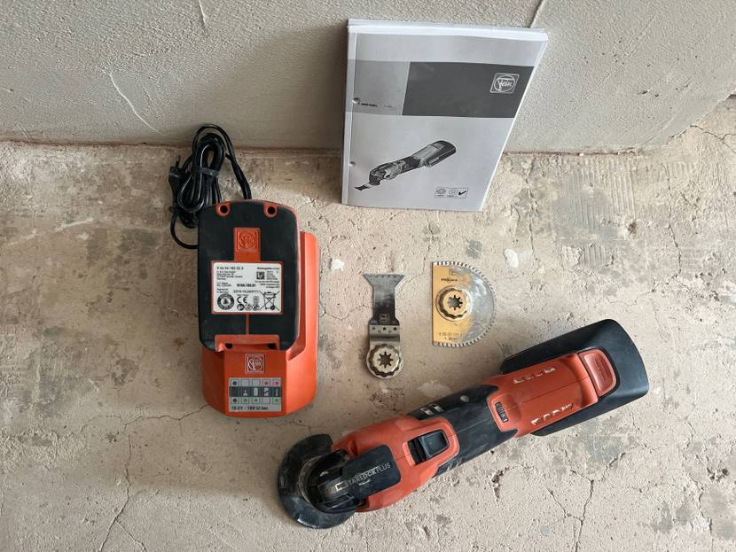 Auf einem Betonboden liegen angeordnet ein getestetes Multitool und sein Zubehör.