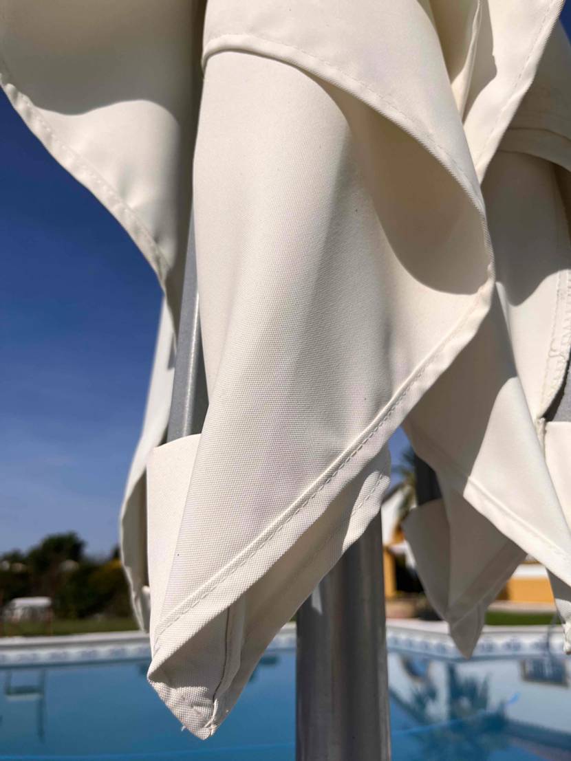 Sonnenschirme im Test: Detailansicht der Nähte und des Materials sowie des Aluminium-Gestells eines weißen Sonnenschirms am Swimmingpool.