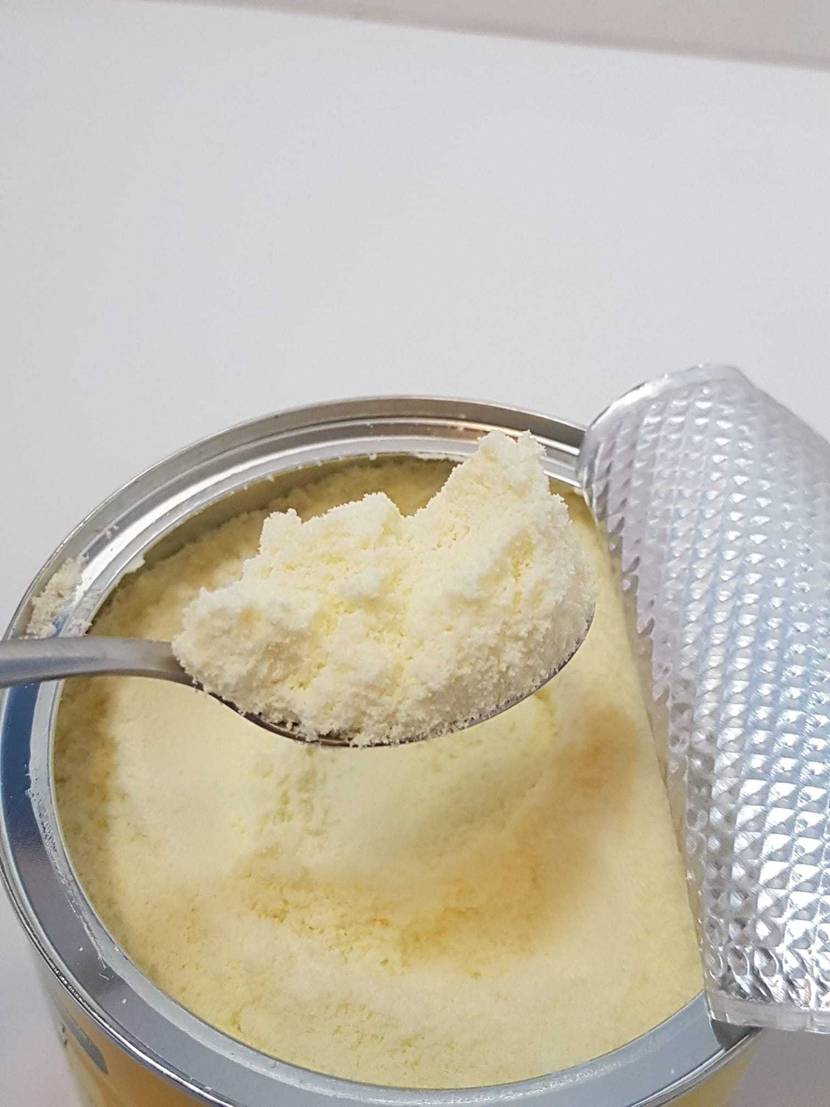 Ein Löffel mit Pulver über einer Dose des getesteten Milchpulvers auf einer hellen Oberfläche.
