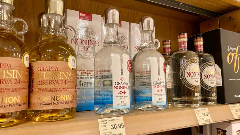 Grappa getestet: Zwei Flaschen stehen vor ihrem Originalkarton mit mehreren anderen Spirituosen in einem Verkaufsregal inklusive Preisangaben.