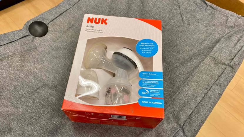 Eine NUK Handmilchpumpe im Test liegt innerhalb ihrer Verpackung mit Sichtfenster auf einer grauen Decke.