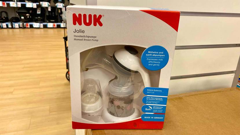 Eine Verpackung mit Sichtfenster, hinter dem sich eine getestete Handmilchpumpe von NUK inklusive Zubehör befindet, ist in einem Geschäft ausgestellt.