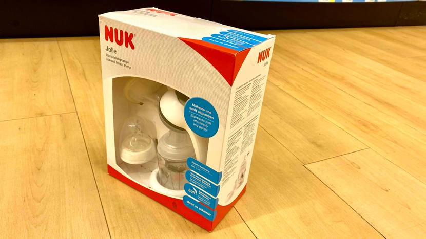 Im Test: Eine NUK Handmilchpumpe steht inklusive Zubehör in ihrer Originalverpackung mit Produktbeschreibung und Anwendungstipps auf einem Parkett.