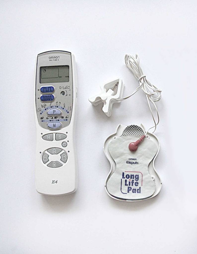 Das Reizstromgerät im Test liegt neben dem Kabel und den Pads auf einer weißen Oberfläche.