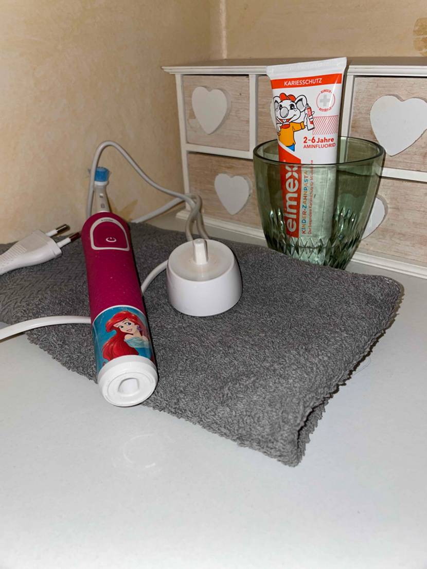 Elektrische Kinderzahnbürste mit Akku, Zahnpasta, Becher und Handtuch im Badezimmer.