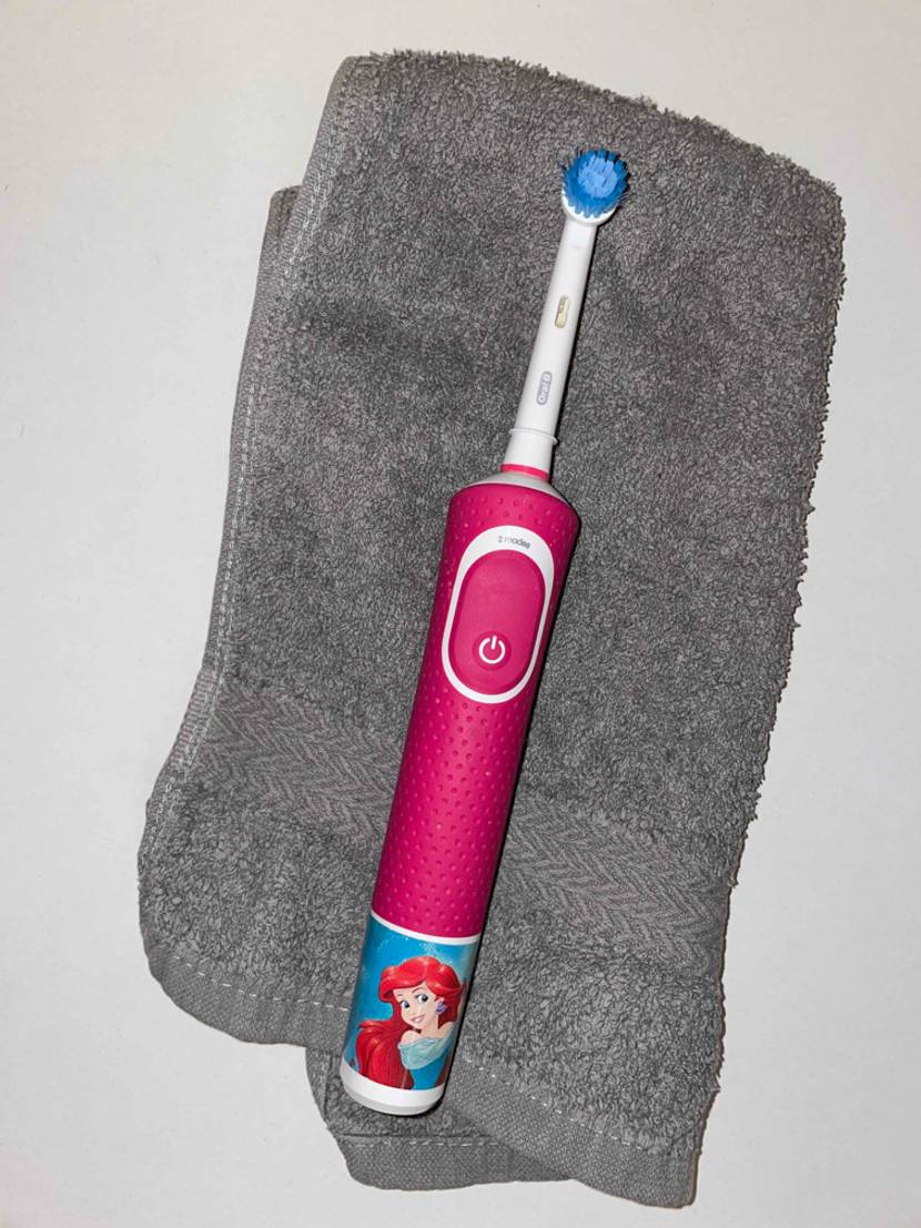 Elektrische Kinderzahnbürste liegt auf einem grauen Handtuch.