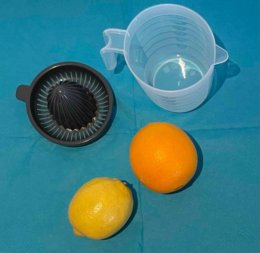 Getestete Orangenpresse-Zitruspresse befindet sich zusammen mit den Früchten auf einer blauen Oberfläche.
