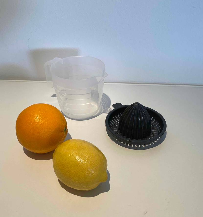 Aufsatz und Behälter von einer getesteten Orangenpresse-Zitruspresse befindet sich zusammen mit den Früchten auf dem Küchentisch.