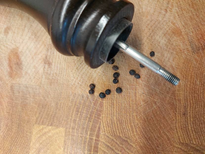 Pfeffermühle getestet: Eine Mühle ohne Deckel mit Pfefferkörnern auf einer Holzfläche.