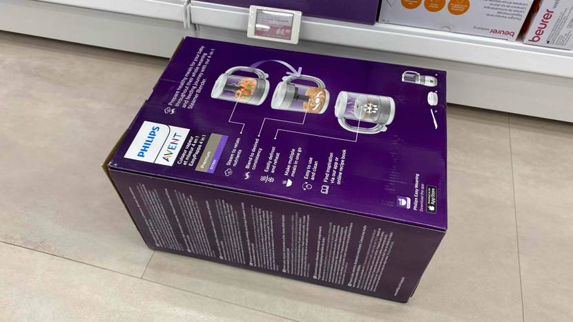 Im Test: Die Rückseite eines originalverpackten Babynahrungszubereiter vor einem Regal auf einem Fließenboden liegend.