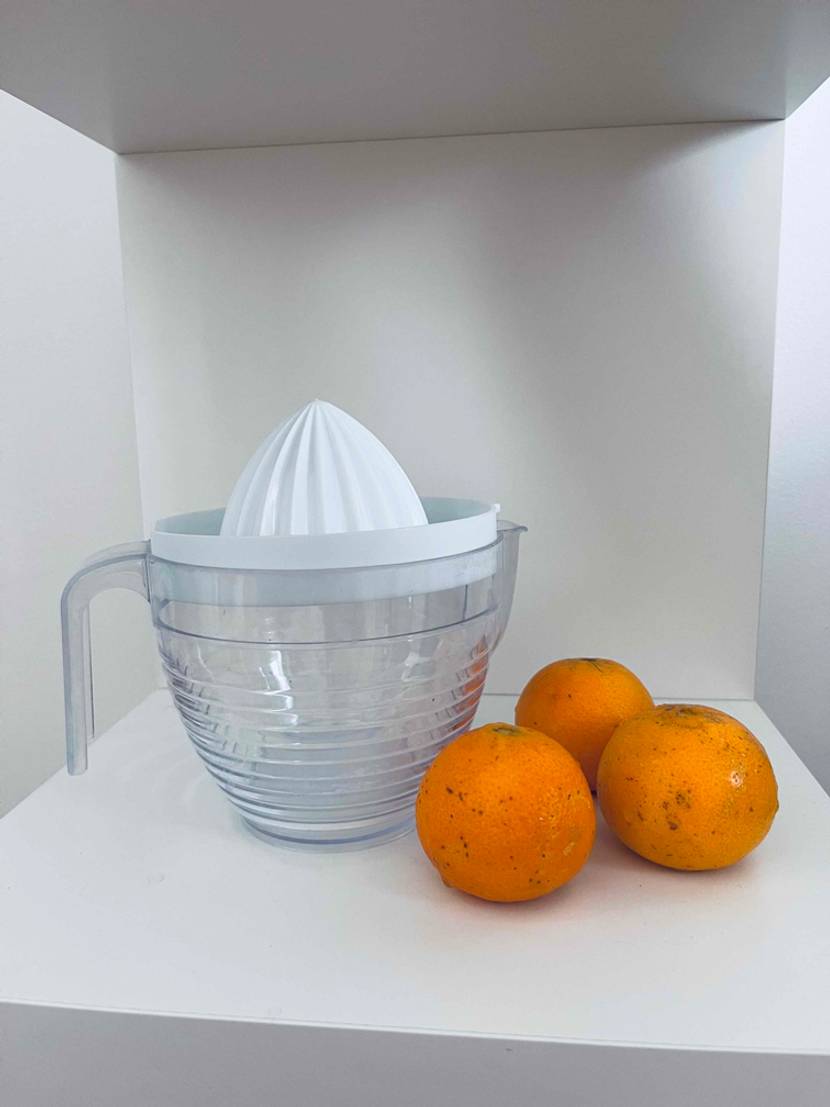 Getesteter Entsafter aus Plastik steht neben drei Orangen.