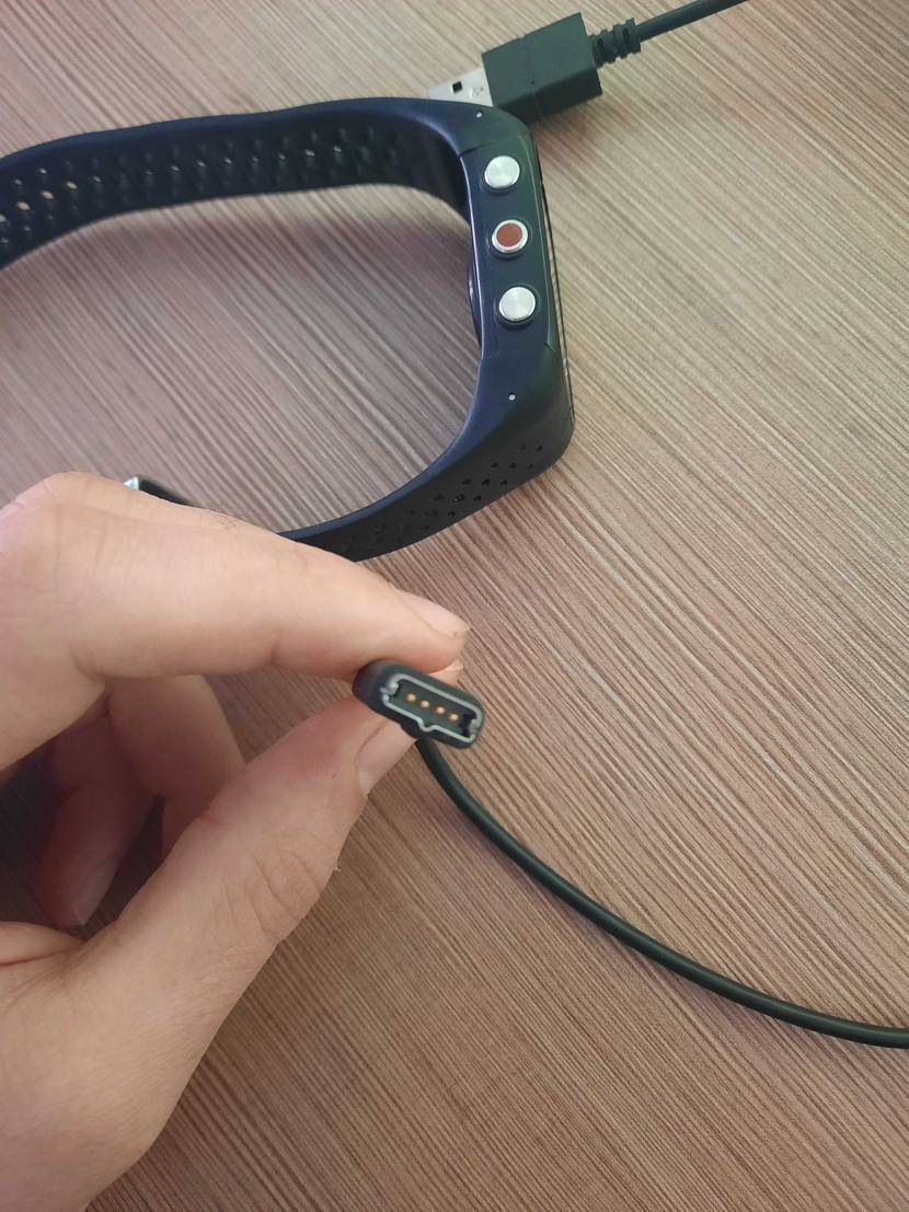 Eine Hand hält einen Stecker der Polar-Pulsuhr im Test die dahinter liegt.
