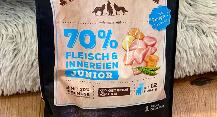 Nahaufnahme einer Verpackung inklusive getreidefreiem, mit Gemüse angereichertem Fleisch Welpenfutter im Test vor einem Langhaarteppich.