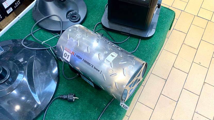 Ansicht von oben auf einen getesteten Gasheizstrahler in Form eines Metall-Zylinders, der Marke ROWI HGH 10000/3 Inox, der auf einem grünen Kunstrasen mit anderen Heizstrahlern steht.