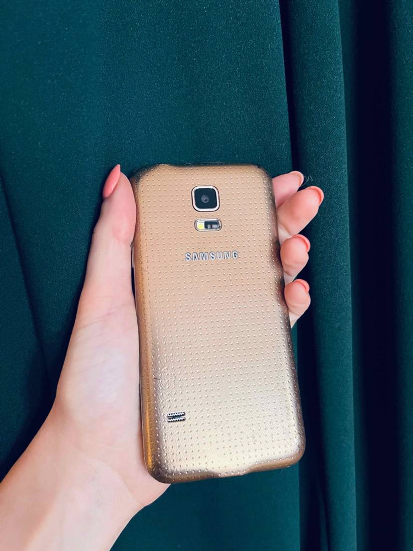 Kleine Smartphones im Test: ein goldenes Modell von Samsung wird von einer Hand vor einen dunkelgrünen Vorhang gehalten.