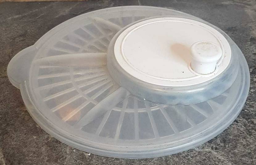 Ein transparenter Kunststoff-Deckel mit weißer Schleuderkurbel von einer getesteten Salatschleuder liegt mit der Unterseite auf einer grauen Marmorplatte.