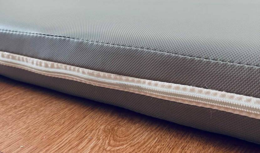 Matratzen im Test: Detailansicht des Reissverschlusses von einer Schaummatratze mit grauem Bezug, die auf einer Holzfläche liegt.