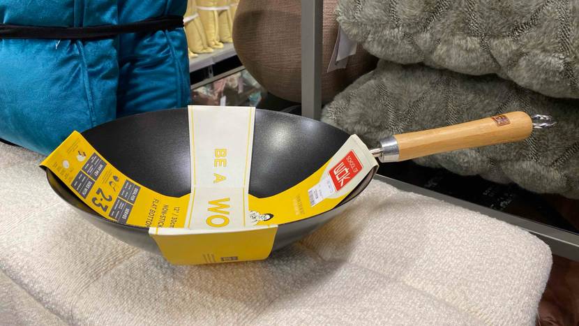Im Test: Wok im grauen Design inklusive Holzgriff liegt in seiner Originalverpackung auf hellem Untergrund in einem Verkaufsbereich.