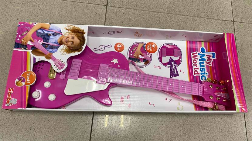 Kindergitarre im Test: rosa Gitarre liegt in Verpackung mit Mädchenfoto auf dem Boden.