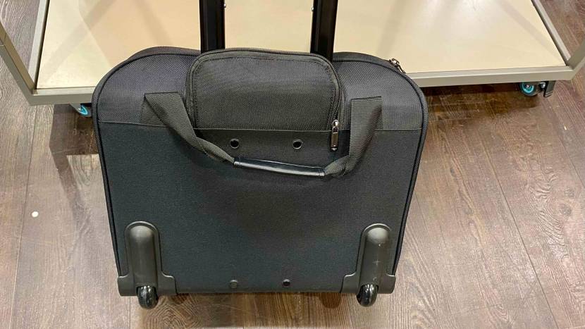 Pilotenkoffer-Test: Ansicht von hinten auf ein Softcase-Modell aus schwarzem Gewebe mit ausgefahrenem Griff auf einem Holzboden vor einem beigefarbigen Regal.