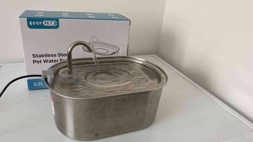 Getesteter Katzenbrunnen mit eingeschaltetem Wasserstrahl steht ausgepackt vor der Verpackung auf weißem Hintergund.