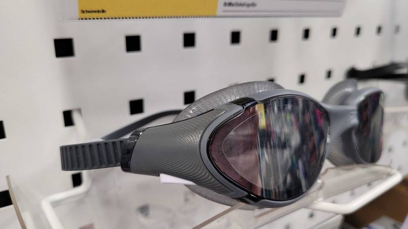 Detailansicht von der Seite auf eine graue Speedo Biofuse Schwimmbrille im Test, die über getönte Kunststoffgläser verfügt und in einem Ausstellungsbereich liegt.