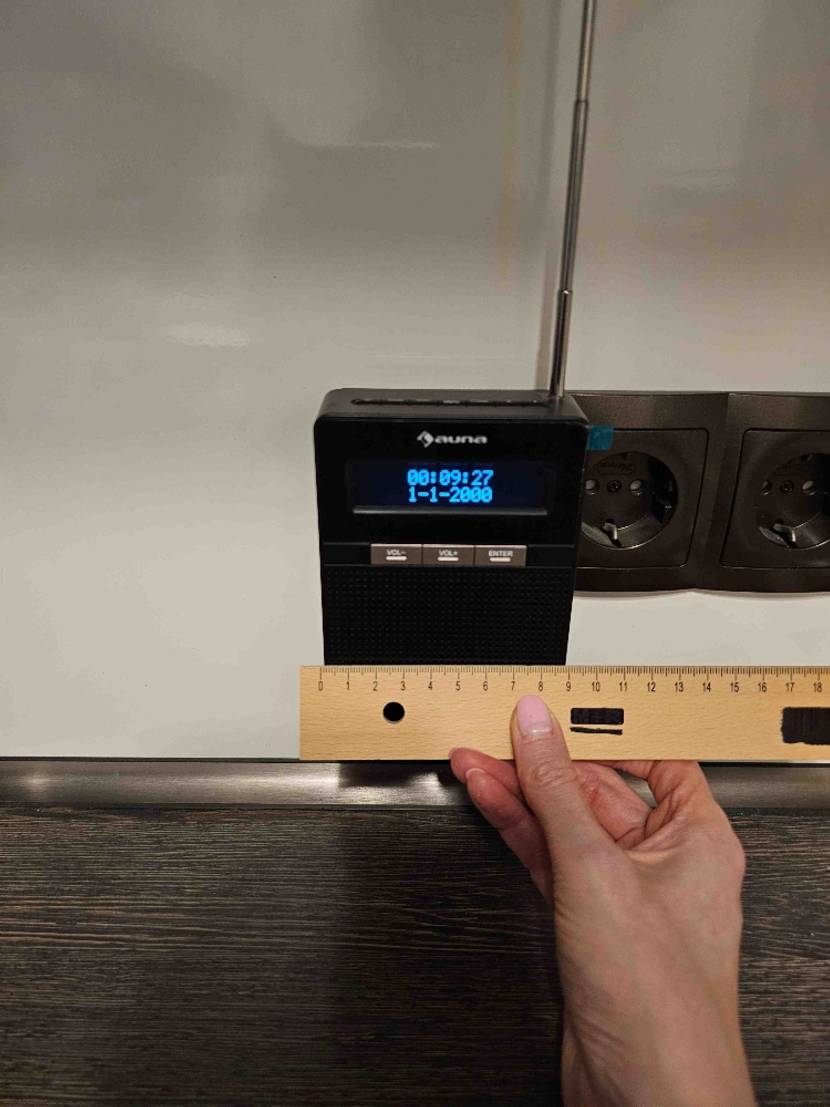 Im Test: Eine Hand hält ein Lineal an das Steckdosenradio in der Steckdosenleiste an der Wand.