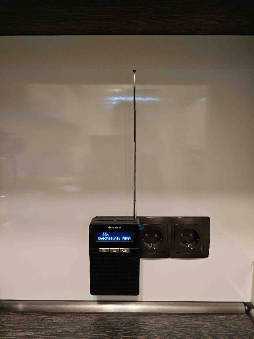 Steckdosenradio getestet: Ein Radio in einer dunklen Steckdosenleiste an einer hellen Wand.